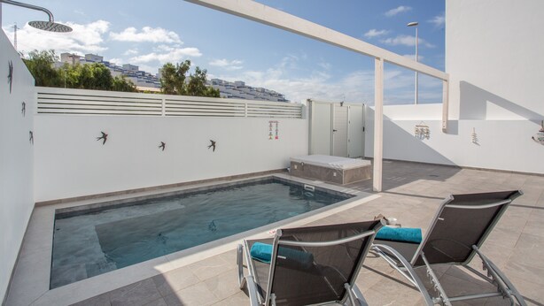 A rooftop swimming pool with lounge chairs, a water feature, and a view of buildings in the background. - Holiday Home 'Gara Fuerteventura' with Pool, Wi-Fi and Air Conditioning (Gran tarajal)