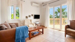 Una sala de estar con sofá, mesa de centro, televisor y balcón con vistas a palmeras.