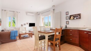Una sala de estar con sofá, una mesa de comedor con sillas, televisor y una cocina con alacenas y mostrador.