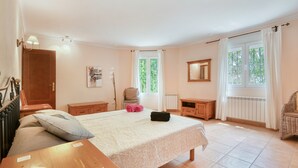 Un dormitorio con cama, mesitas de noche, una silla, un ventanal con cortinas y un radiador.
