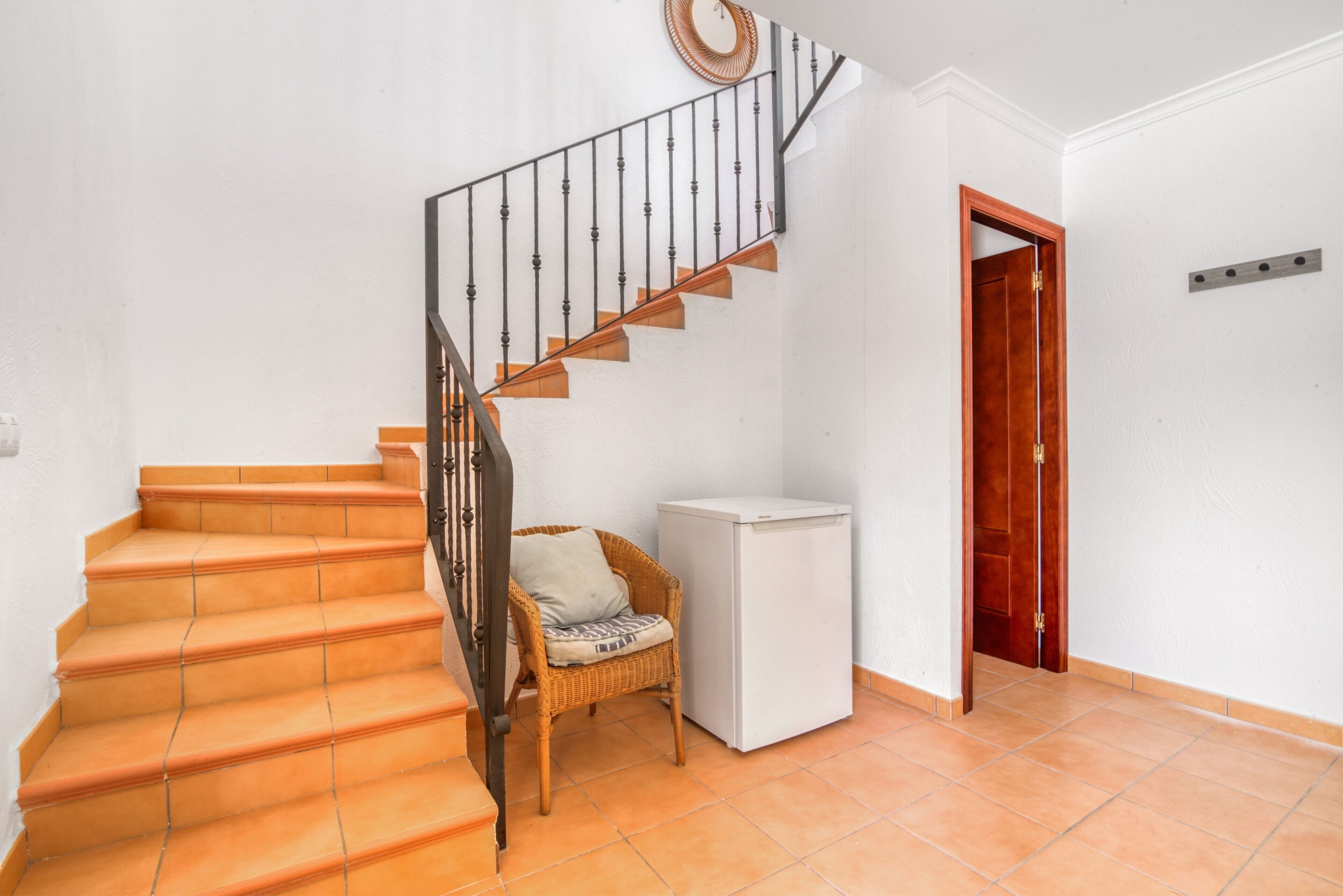 A staircase with orange steps, a wicker chair, a white cabinet, and a wooden door.