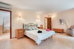 Um quarto com cama, mesas de cabeceira, uma cadeira, um armário de madeira e uma escada.