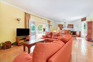 Ein Wohnzimmer mit Sofa, Fernseher und einer Küchenzeile im Hintergrund.