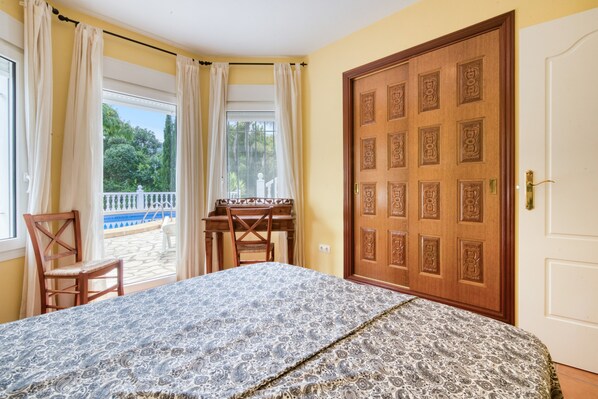 A bedroom with a large bed, a wooden door, a window with curtains, and a view of a balcony.