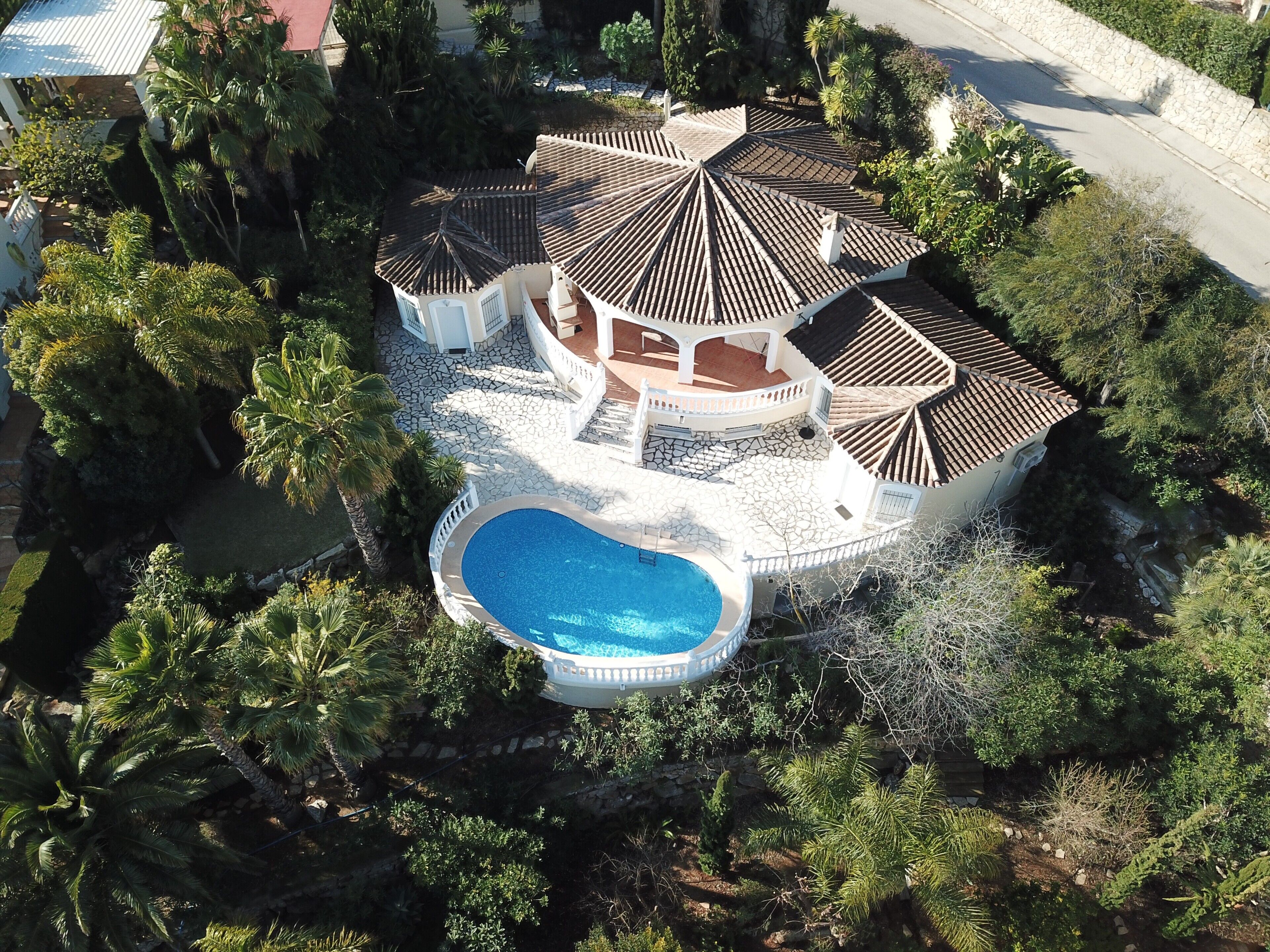 A large house with a swimming pool, surrounded by lush greenery and multiple tiled-roofed structures.
