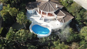 Ein großes Haus mit Swimmingpool, umgeben von üppiger Vegetation und mehreren Gebäuden mit Ziegeldächern.