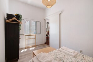 Une chambre à coucher avec un lit, une commode en bois, un miroir et une plante suspendue.
