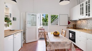 A compact kitchen with white cabinets, a dining table with a patterned tablecloth, and a view through an open door to a balcony.