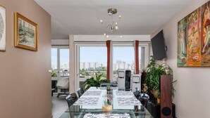Un espace de salle à manger moderne, avec une table en verre, des chaises, un lustre et des œuvres d’art accrochées aux murs.