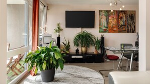 Un salon moderne doté d’un téléviseur à écran plat, d’un coin repas avec une table en verre et d’une grande plante en pot.