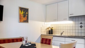 Una cocina con armarios blancos, salpicadero de azulejos y un cuadro de palmeras.