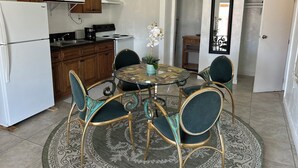 A compact kitchen with a refrigerator, stove, microwave, and wooden cabinets. There is a dining area with a round table and four chairs, and a potted orchid on the table.