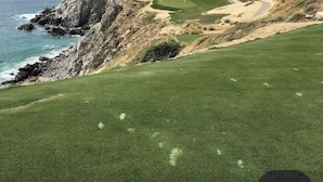 Un campo de golf costero con un acantilado rocoso, una zona arenosa y un césped bien cuidado.