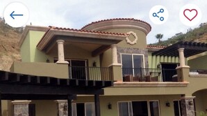 Una casa de dos pisos con balcón, patio cubierto y piscina.