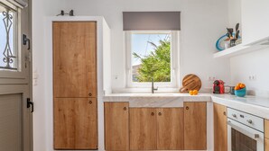 A kitchen with wooden cabinets, a window with a view of greenery, a sink, and a countertop with kitchen utensils. - Country House 'Allegro' with Sea View, Wi-Fi and Air Conditioning (Tinos)