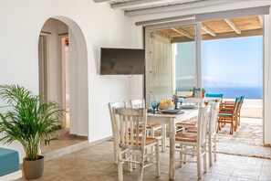 A dining area with a table and chairs, a television, and a view of the sea.