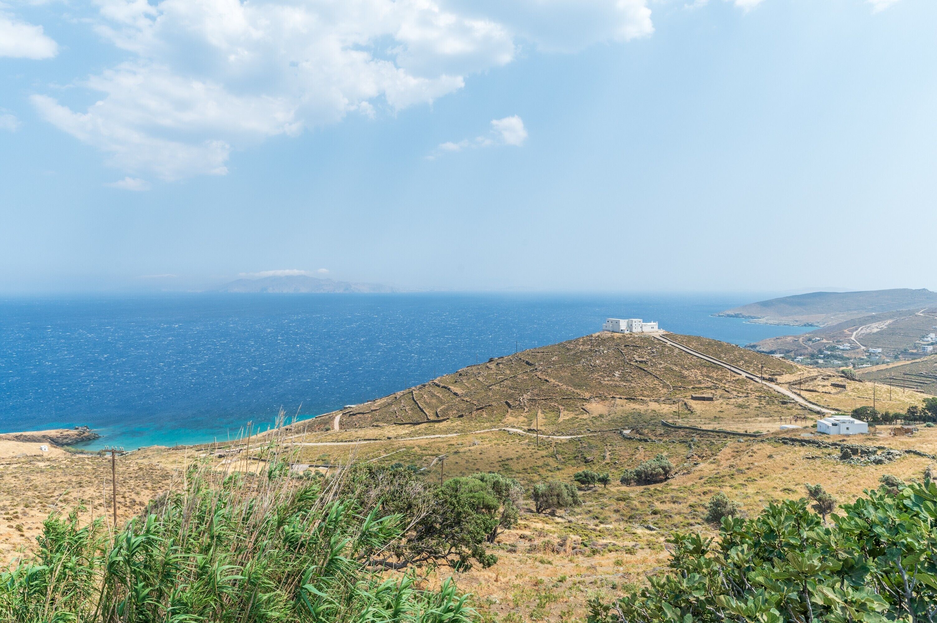 A coastal landscape with a hill, a white building, and a view of the sea.