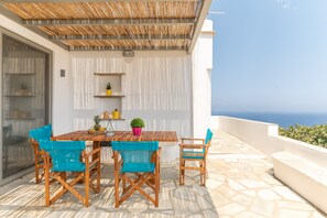 A terrace with a table and chairs, a pergola, and a view of the sea.