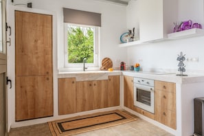 A modern kitchen with wooden cabinets, a built-in oven, a window with a view of greenery, and a countertop with kitchen utensils.