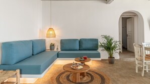 A modern living room with a sectional sofa, a small round table with a plate of food, a hanging lamp, and a potted plant. - Country House 'Allegro' with Sea View, Wi-Fi and Air Conditioning (Tinos)