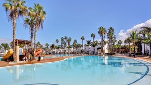 A swimming pool with palm trees, a water slide, and a covered area.