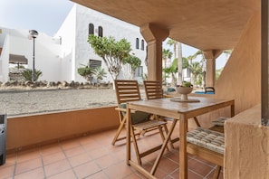 An outdoor patio with a wooden table and chairs, a small plant on the table, and a white building in the background. - Oasis Duna - Casa Amanay: Shared Pool, Private Terrace & Wi-Fi for Your Vacation (Corralejo)