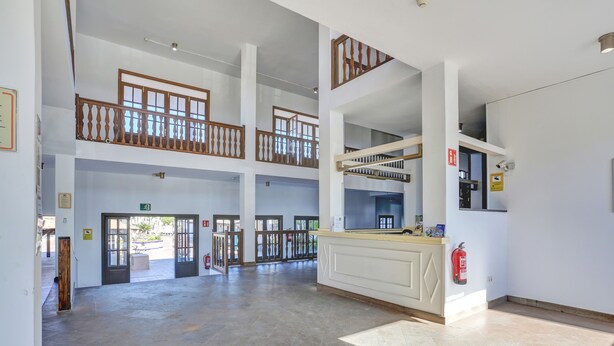 A spacious lobby with a high ceiling, multiple doors, a reception desk, and a fire extinguisher.