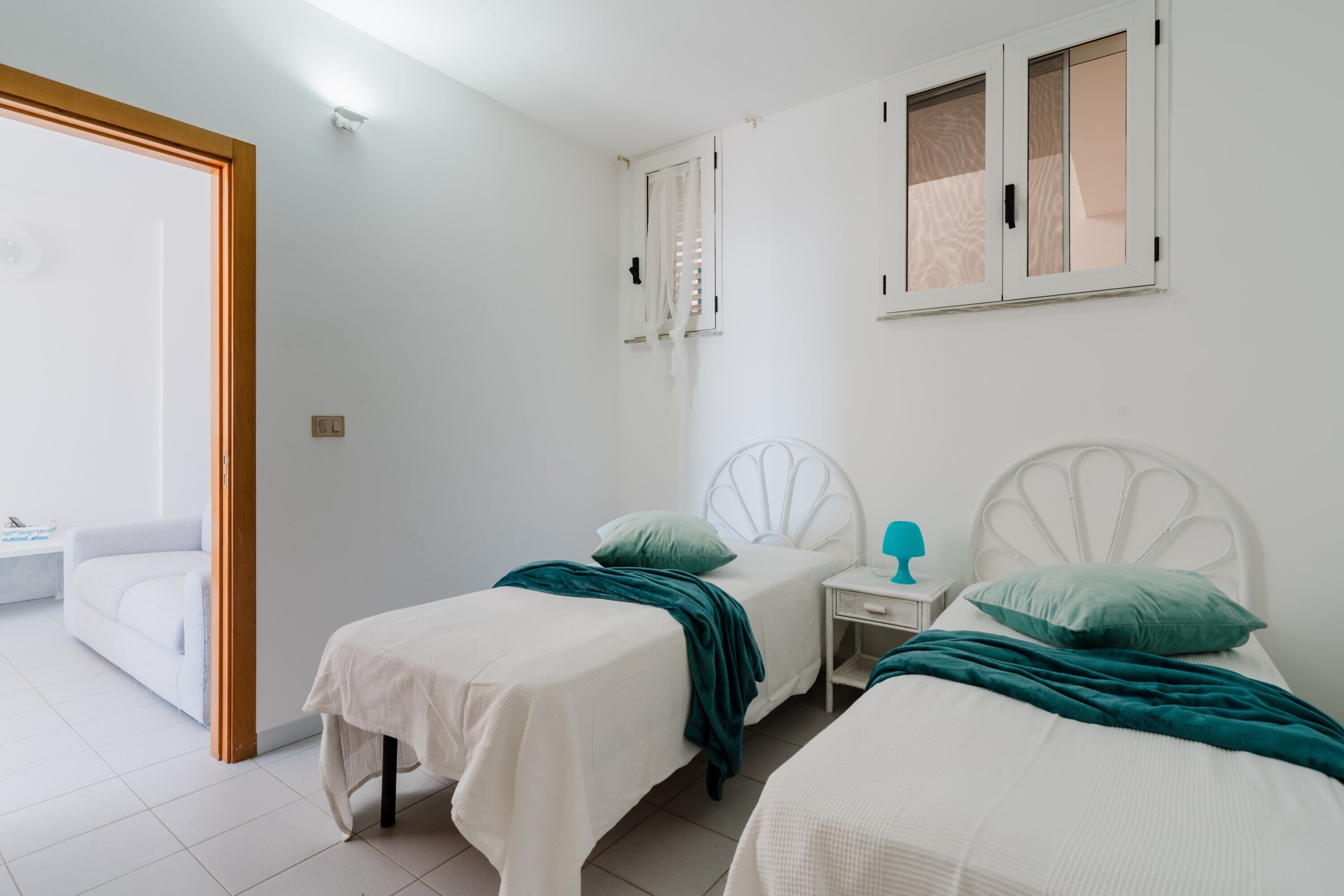A bedroom with two beds, a nightstand, a window, and a door leading to a balcony.