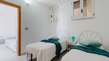 A bedroom with two beds, a nightstand, a window, and a door leading to a balcony.