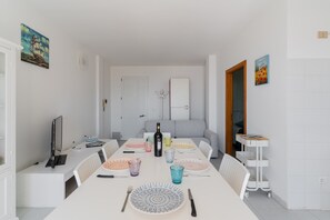 A dining area with a long table, chairs, a bottle of wine, and a television on a stand.