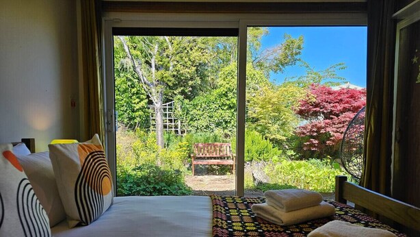 A bedroom with a bed, pillows, a patterned rug, and a view of a garden through a sliding door. - The Robin House in Ravelston (Edinburgh)