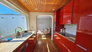 A modern kitchen with red cabinets, wooden flooring, and a central island. - The Robin House in Ravelston (Edinburgh)