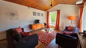A modern living room with a wooden ceiling, a sofa set, a coffee table, and a TV on a wooden cabinet. - The Robin House in Ravelston (Edinburgh)