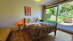 A bedroom with a wooden bed, a small bedside table with a lamp, a poster on the wall, and a large window with a view of greenery outside. - The Robin House in Ravelston (Edinburgh)