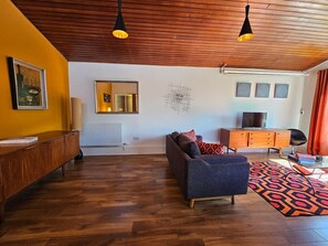A modern living room with wooden flooring, a sofa, a cabinet, and a television.