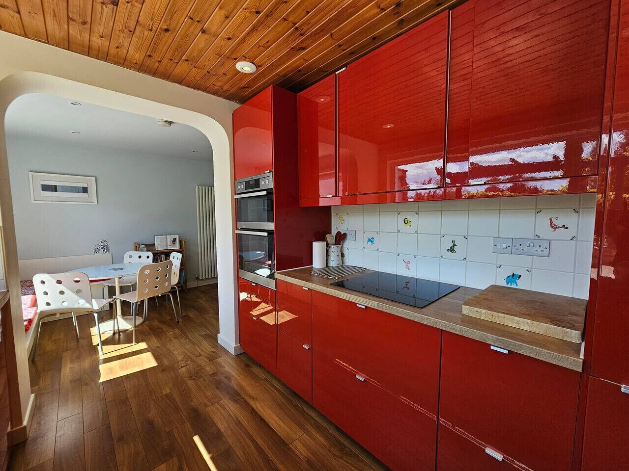 Una cocina moderna con armarios rojos, encimera de madera y comedor con sillas blancas.