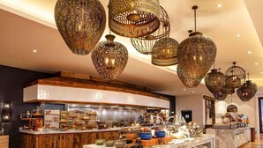 Un hall d’hôtel spacieux, doté d’un comptoir de réception en marbre, d’un comptoir incurvé proposant une sélection de plats et de boissons, et de magnifiques lustres suspendus.
