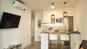 A modern apartment with a kitchen, dining area, and living room. It includes a flat-screen TV, a dining table with chairs, a sofa with cushions, and a small round table. - Playa de la Fontanilla Marbella (Marbella)