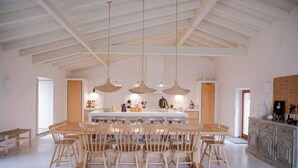 A spacious dining area with a long table and multiple chairs, a kitchen with white cabinets, and pendant lighting. - Charming 3-bedroom cottage in Serra d'Aire (Leiria)
