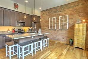 Una cocina moderna con una isla central, taburetes de bar, microondas y pared de ladrillo.