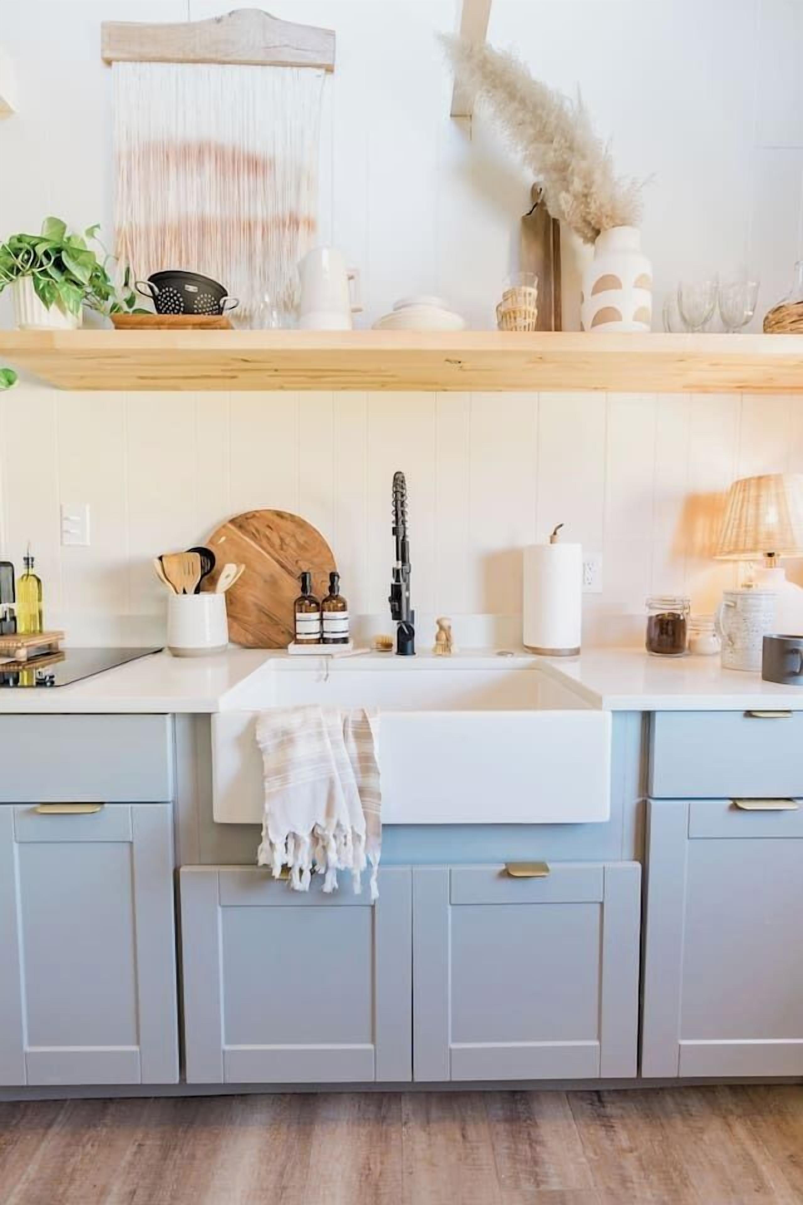 Una cocina moderna con un lavamanos blanco central, estantes de madera arriba y armarios grises claro debajo.