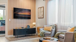 A modern living room with a large TV, a console table, and a comfortable seating area with a sofa and armchairs. - Stone & Flora 2BR Condo Near Downtown and Bay (Traverse City)