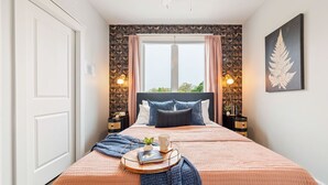 A bedroom with a large bed, two bedside tables, a window with curtains, and a wall-mounted artwork. - Stone & Flora 2BR Condo Near Downtown and Bay (Traverse City)
