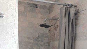 A shower with a stone wall, a metal showerhead, and a grey curtain.