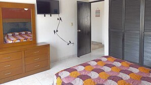 A bedroom with a bed, a dresser, a television mounted on the wall, and a ceiling fan.