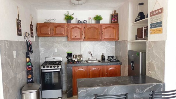 A compact kitchen with wooden cabinets, a gas stove, a refrigerator, and a marble countertop.