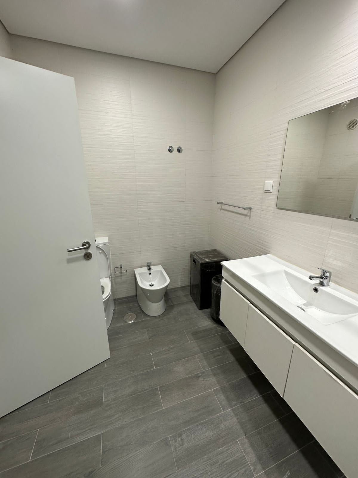 Ein modernes Badezimmer mit einem Bidet, einer Toilette, einem Waschbecken und einem Spiegel.