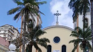 Eine Kirche mit Kuppel und Kreuz, umgeben von Palmen und einem Kopfsteinpflasterhof.