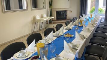 Une longue table à manger, dressée avec des assiettes, des verres et des couverts, entourée de chaises et recouverte d’une nappe bleue.