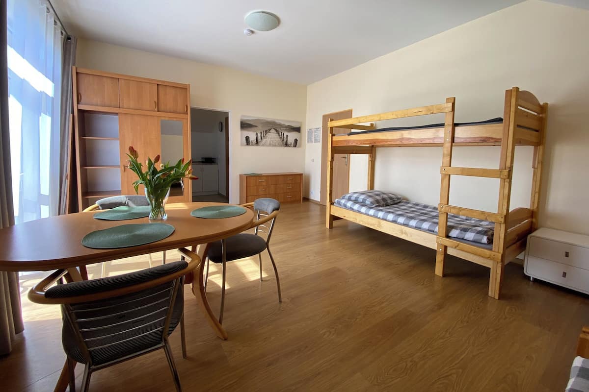 A room with a bunk bed, wooden cabinets, a dining table with chairs, and a small kitchen area.